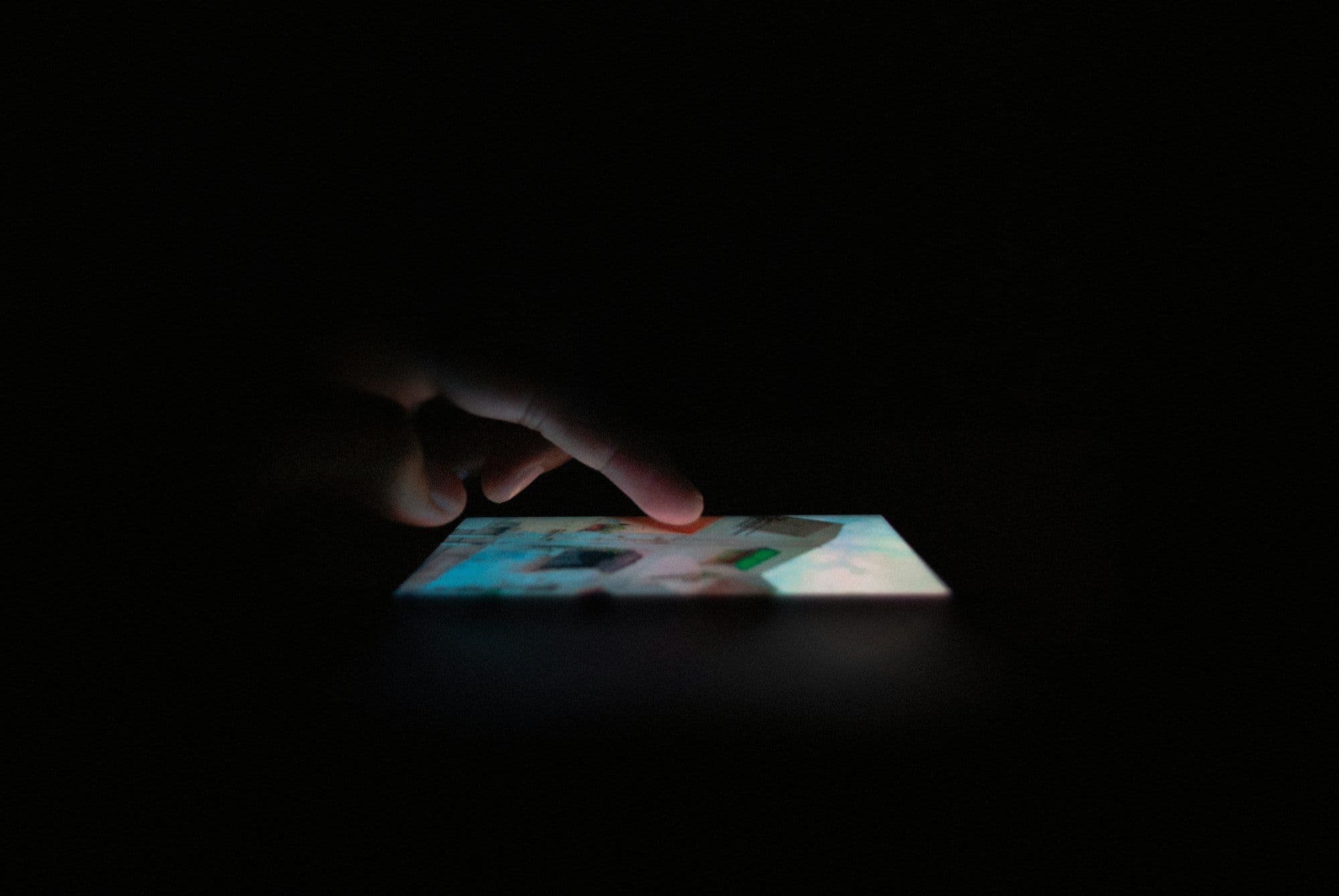 A hand reaching toward a smartphone glowing with app icons in the dark
