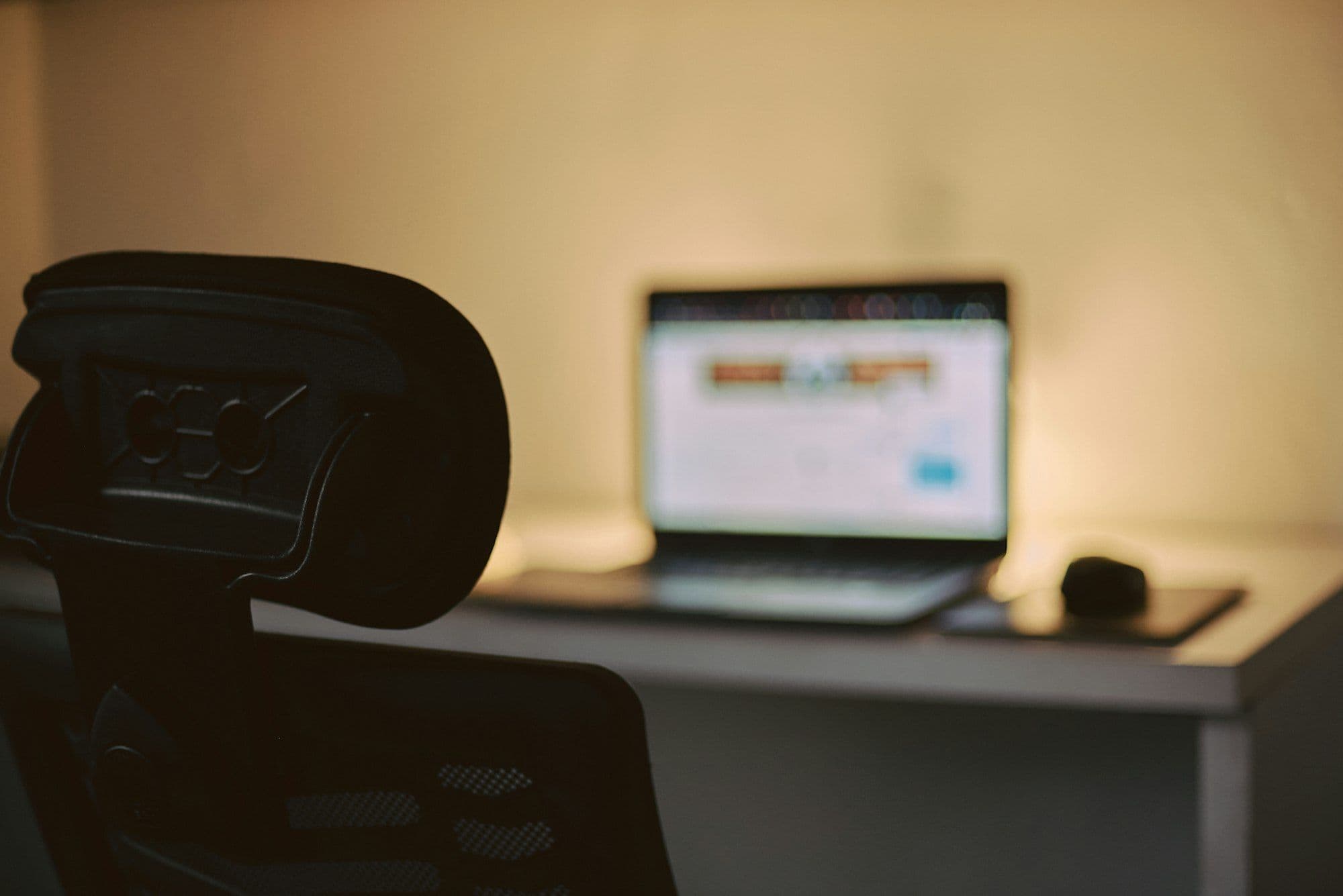 A laptop showing a website open on a desk in a dimly lit home office