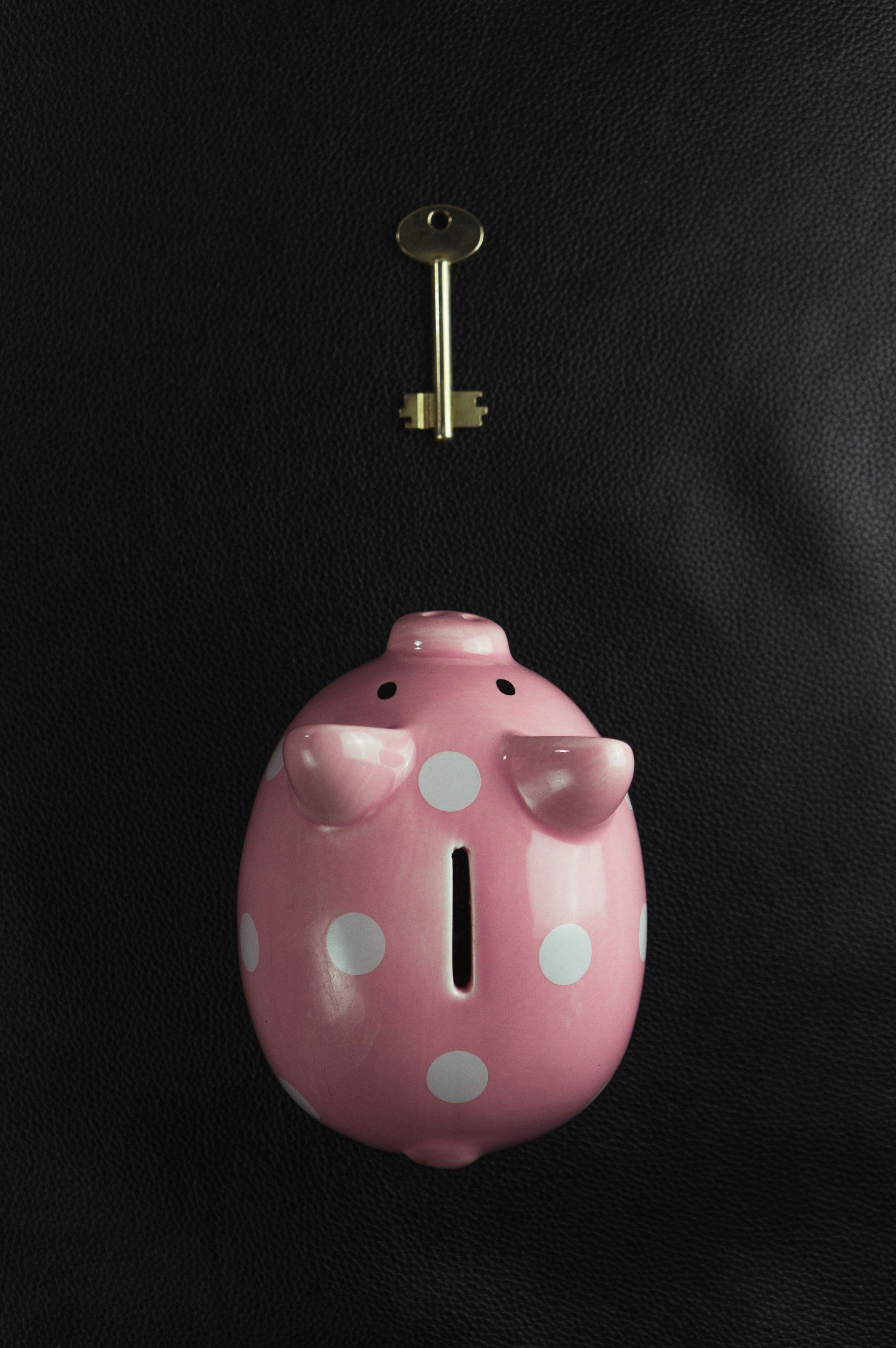 A pink piggy bank and a small brass key on a dark background